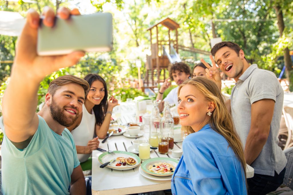 Portrait of a cheerful friends making selfie photo on smartphone in outdoor restaurant